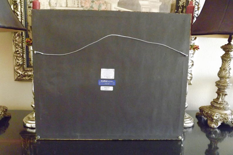 May include: The back of a framed picture with a black mat and a gold frame. A small blue label with white text is attached to the back of the frame. The label reads "Sterling Classics".