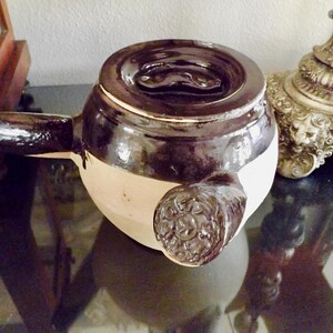 May include: A black and white ceramic teapot with a lid and a spout. The teapot has a decorative design on the side.