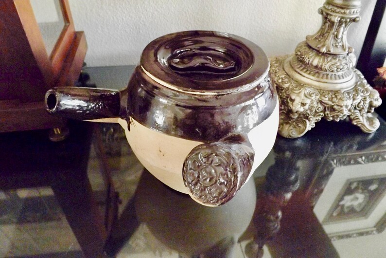 May include: A black and white ceramic teapot with a lid and a spout. The teapot has a decorative design on the side.