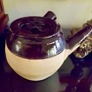 May include: A brown and white ceramic teapot with a lid and a spout. The teapot has a glossy brown glaze on the top half and a matte white glaze on the bottom half.