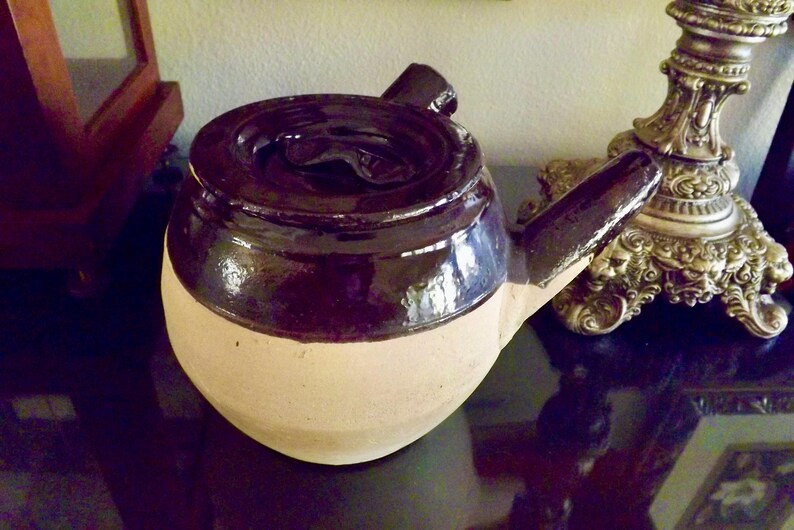 May include: A brown and white ceramic teapot with a lid and a spout. The teapot has a glossy brown glaze on the top half and a matte white glaze on the bottom half.