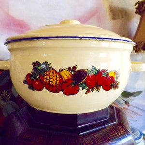 May include: A white enamelware casserole dish with a lid. The dish has a blue rim and a colorful fruit design featuring pineapples, lemons, and tomatoes.