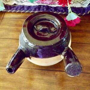 May include: A black ceramic teapot with two spouts and a white mustache design on the lid.