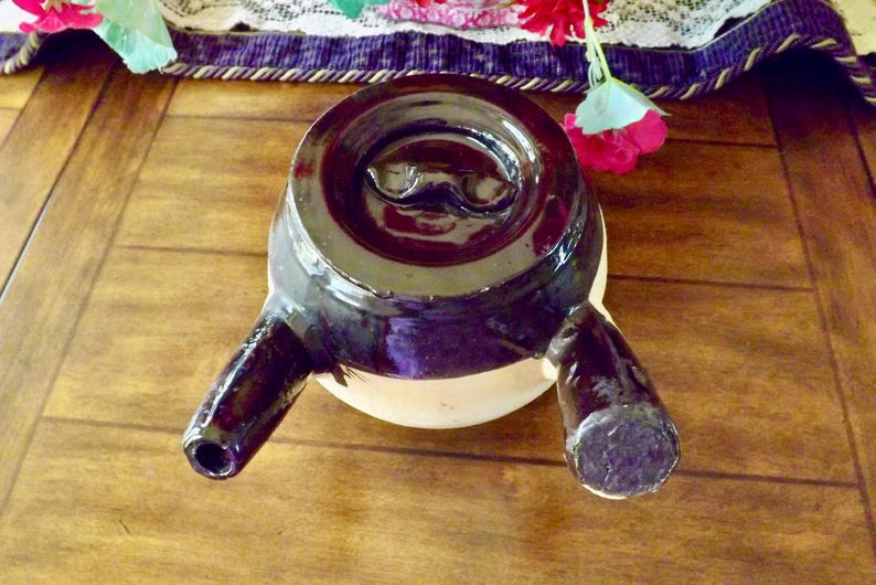 May include: A black ceramic teapot with two spouts and a white mustache design on the lid.