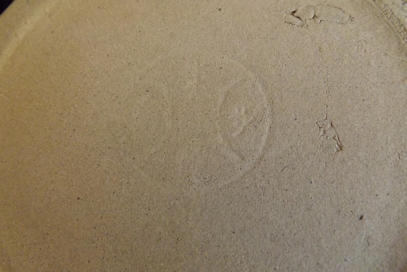 May include: Close-up of a light brown ceramic surface with a faint, circular mark in the center.