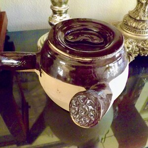 May include: A brown and white ceramic teapot with a spout and a handle. The teapot has a dark brown glaze on the top and a lighter brown glaze on the bottom.