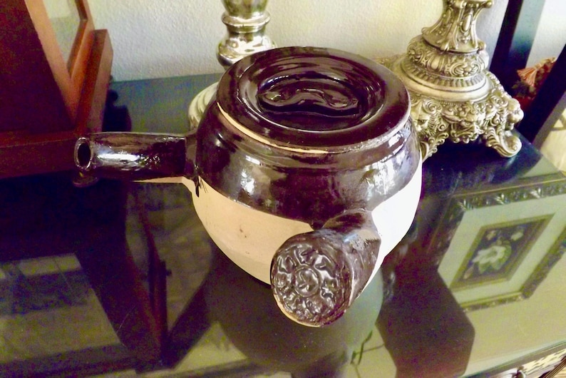 May include: A brown and white ceramic teapot with a spout and a handle. The teapot has a dark brown glaze on the top and a lighter brown glaze on the bottom.