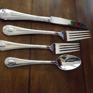 May include: A set of four silver-plated flatware pieces, including a knife, fork, and spoon. The handles are decorated with a beaded pattern and a small oval design.