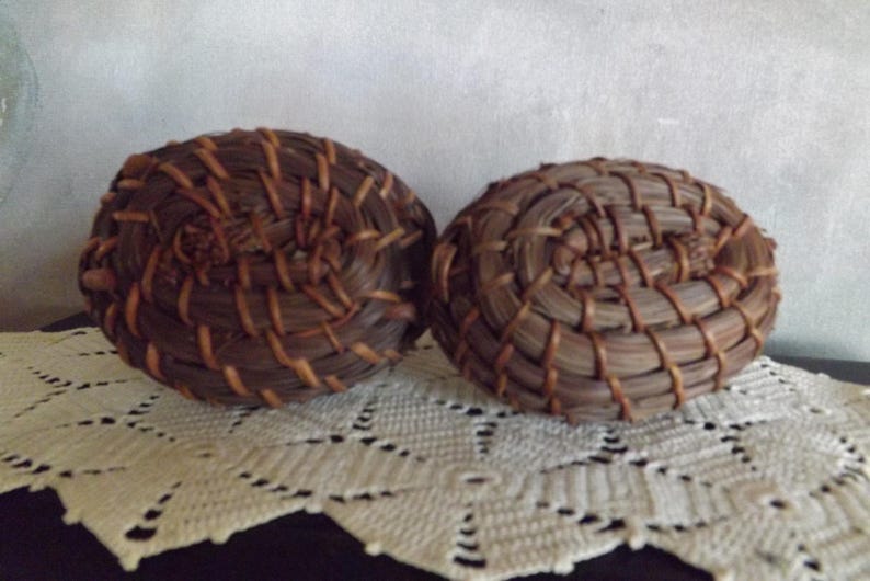 Puede incluir: Dos cestas redondas tejidas con fibras naturales marrones y beige. Las cestas est&aacute;n colocadas una al lado de la otra sobre un tapete blanco de encaje. Las cestas tienen un dise&ntilde;o en espiral y probablemente est&aacute;n hechas a mano.