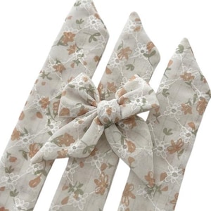 May include: Three beige fabric hair ties with a floral pattern. The hair ties are tied together in a bow.