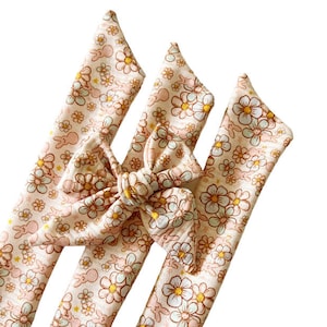 May include: Three fabric headbands with a floral and bunny print in shades of pink, yellow, and brown. The headbands are tied together in a bow.