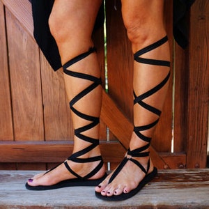 K&ouml;nnte beinhalten: Schwarze Sandalen mit mehreren Riemen, die sich um die Kn&ouml;chel und Waden wickeln.