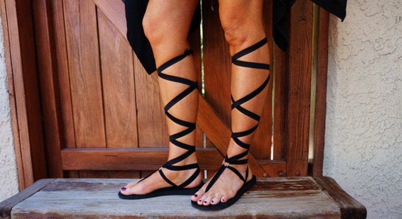 K&ouml;nnte beinhalten: Schwarze Sandalen mit mehreren Riemen, die sich um die Kn&ouml;chel und Waden wickeln.