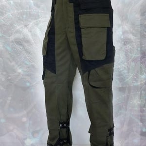 May include: Green cargo pants with black accents and adjustable straps at the ankles. The pants have multiple pockets and a belt loop.