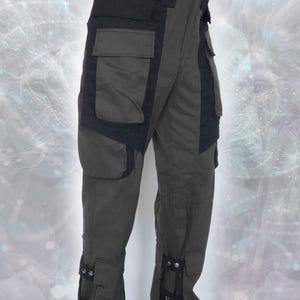 May include: Dark green cargo pants with black accents and multiple pockets. The pants have adjustable straps at the bottom of the legs.