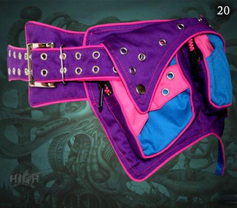 May include: A purple and pink fabric belt with a blue pocket and multiple silver eyelets. The belt has a large silver buckle and a pink trim.