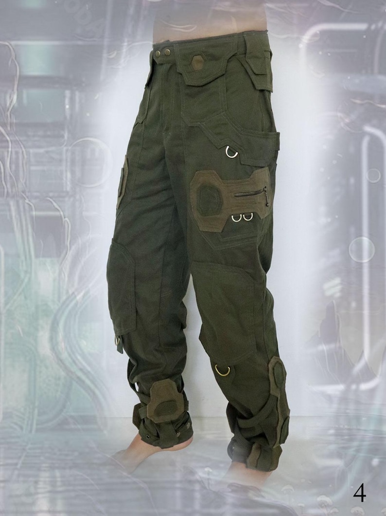K&ouml;nnte beinhalten: Gr&uuml;ne Cargohose mit mehreren Taschen und Riemen. Die Hose hat ein einzigartiges Design mit einem gro&szlig;en Patch am rechten Oberschenkel und Riemen um die Kn&ouml;chel.