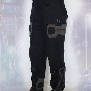 K&ouml;nnte beinhalten: Schwarze Cargohose mit grauen Akzenten und mehreren Taschen. Die Hose hat ein einzigartiges Design mit verst&auml;rkten Knien und einer Rei&szlig;verschlusstasche am rechten Bein.