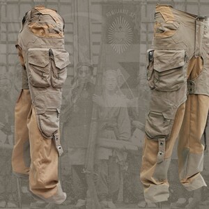 Pu&ograve; includere: Un paio di pantaloni cargo beige con pi&ugrave; tasche e un pannello marrone sulla parte inferiore delle gambe. I pantaloni hanno una tasca con cerniera sulla coscia destra e una cinghia con fibbia sulla coscia sinistra.