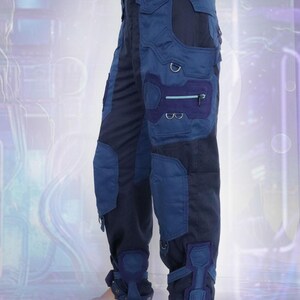 K&ouml;nnte beinhalten: Blaue und schwarze Cargohose mit mehreren Taschen und Riemen. Die Hose hat ein futuristisches Design und ist aus strapazierf&auml;higem Stoff gefertigt.
