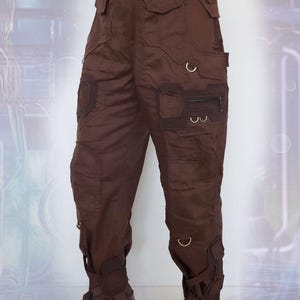 K&ouml;nnte beinhalten: Braune Cargohose mit mehreren Taschen und Schnallen. Die Hose hat eine lockere Passform und eine leicht verk&uuml;rzte L&auml;nge.