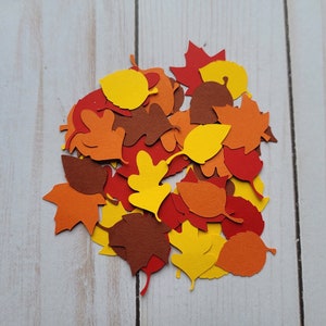 May include: A pile of autumn-themed paper leaves in various shades of orange, yellow, and brown. The leaves are cut out in different shapes, including maple, oak, and simple leaf shapes.