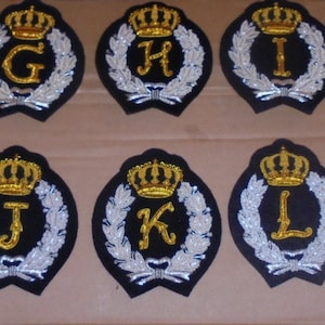 May include: Six embroidered patches with a gold crown and a letter from G to L on a black background. The letters are surrounded by a silver wreath.