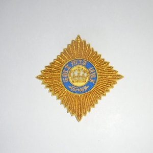 May include: A gold embroidered star with a blue and gold circular emblem in the center. The emblem features a crown and the text "GOET MIT UNS".