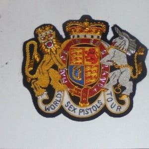 May include: A black embroidered patch with a gold lion and a white unicorn on either side of a royal coat of arms. The patch has the text "World Sex Pistols Tour" around the edge.