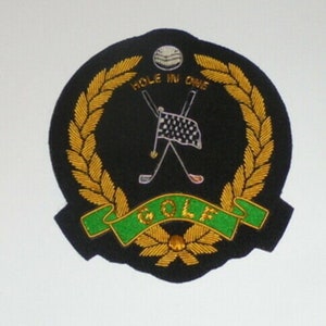 May include: A black and gold embroidered patch with a golf club, golf ball, and the text "HOLE IN ONE GOLF".