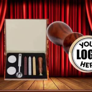 May include: A wooden handle wax seal stamp with a gold-colored metal base. The base has a round, black and white design with the text "YOUR LOGO HERE". The stamp is next to a wooden box with a white interior and a variety of wax seal supplies.