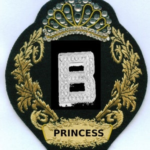 May include: A black and gold embroidered patch with a crown, a letter B made of rhinestones, and the word "PRINCESS" in gold lettering.