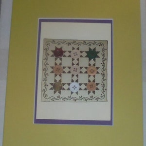 May include: A framed print of a quilt with a button design. The quilt is made of white fabric with brown and tan buttons sewn on in a grid pattern. The buttons are surrounded by a brown and tan floral border.