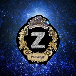 May include: A black and gold embroidered patch with a large silver letter Z adorned with rhinestones. The patch features a crown with pearls and the word "Princess" at the bottom.