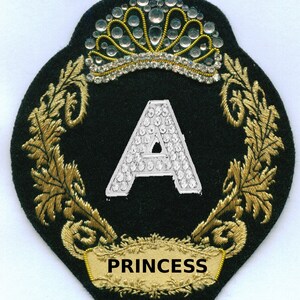 May include: A black and gold embroidered patch with a jeweled crown, the letter A, and the word "PRINCESS".