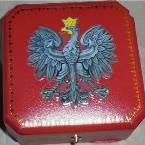 May include: A red box with a gold trim and a white eagle with a gold crown on the lid. The eagle is the national symbol of Poland.