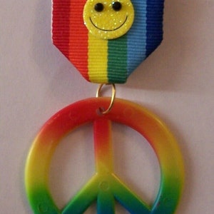 May include: A rainbow peace sign with a yellow smiley face on a rainbow ribbon.