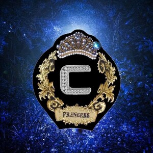 May include: A black and gold embroidered patch with a large letter C surrounded by a crown and a wreath. The patch has the word "Princess" written on it.