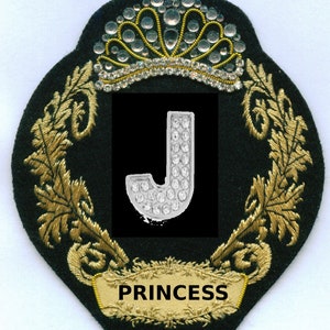 May include: A black and gold embroidered patch with a crown, a letter J made of rhinestones, and the word "PRINCESS" in a banner.