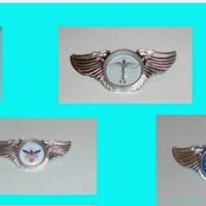 May include: A collection of ten silver and gold winged pins with various logos. The logos include a winged airplane, a medical symbol, a globe, and a stylized bird.