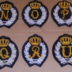 May include: Six embroidered patches with gold crowns and letters N, O, P, Q, R, and U on a dark blue background with silver leaf accents.