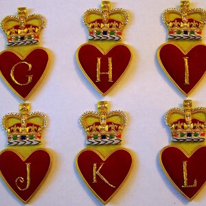 May include: Six red felt hearts with gold crowns and gold letters G, H, I, J, K, and L. The hearts are on a white background.