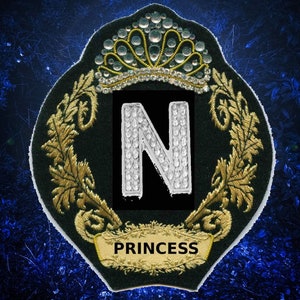 May include: A black and gold embroidered patch with a large letter N made of rhinestones. The patch has a crown above the letter and the word "PRINCESS" below it.