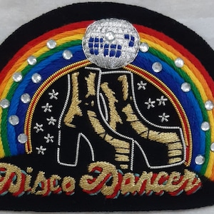 May include: A black felt patch with a rainbow, a silver disco ball, and two gold embroidered platform shoes. The text "Disco Dancer" is embroidered in gold below the shoes.