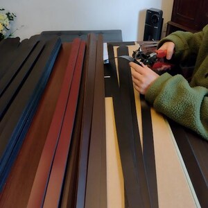 Puede incluir: Varias tiras de cuero en diversos colores, incluyendo negro, marr&oacute;n y burdeos, dispuestas sobre una mesa. Una persona est&aacute; usando una herramienta para trabajar el cuero. Las tiras parecen ser para proyectos de artesan&iacute;a o marroquiner&iacute;a.