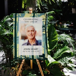 May include: A memorial sign with a forest background, a photo of a man, and the text "Celebrating the life of John Heart, May 20, 1940 - June 30, 2020".