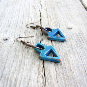 Op de afbeelding: Een paar blauwe driehoekige oorbellen met een koperen draadlus. De oorbellen liggen op een houten oppervlak.