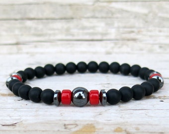 May include: A black beaded bracelet with red and silver accents. The bracelet has a large, round, silver bead in the center.