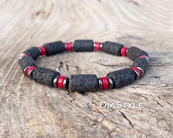May include: A black lava stone bracelet with red and silver accents. The bracelet features cylindrical black lava beads separated by red and silver beads. The bracelet is displayed on a wooden surface. The text "DIASTYLE" is visible.