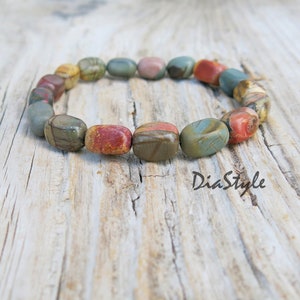 May include: A bracelet made of colorful, patterned stones. The stones are oval-shaped and have a smooth, polished finish. The bracelet is on a wooden surface.